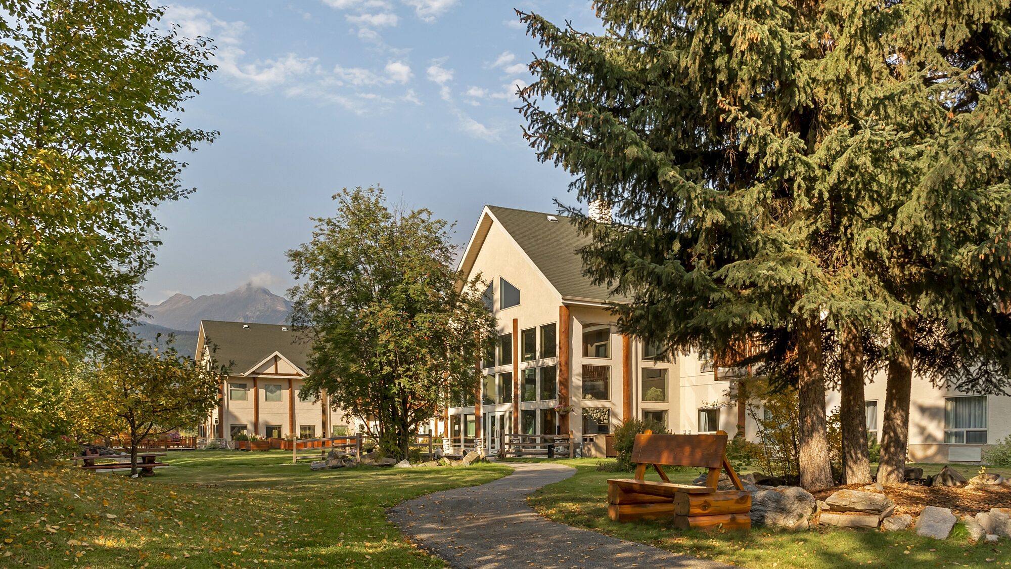 Exterior of Best Western Plus Valemount featuring a paved path, lush lawn, and mountain views under a blue sky.