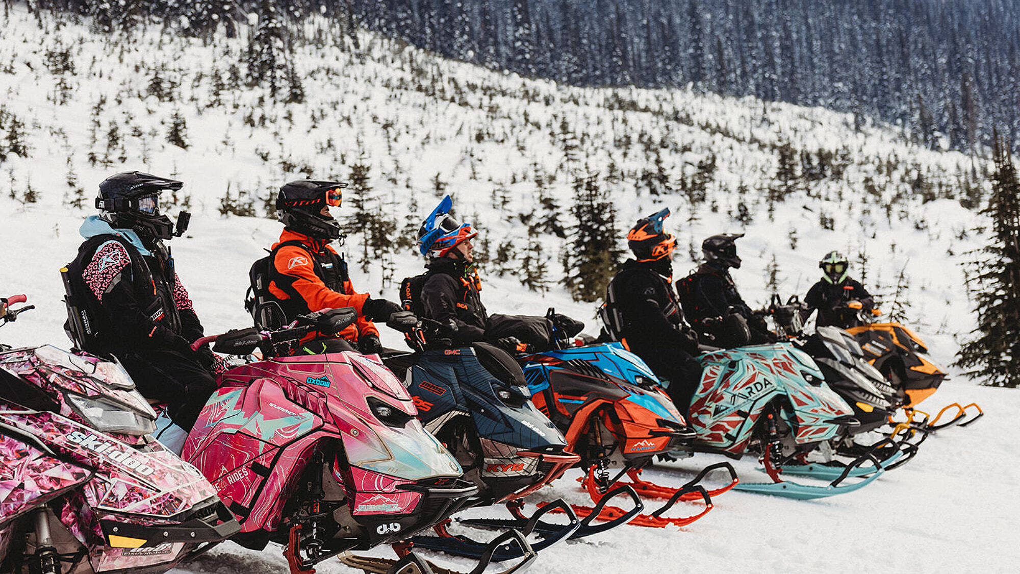 Group of people wearing helmets riding snowmobiles across a snowy landscape