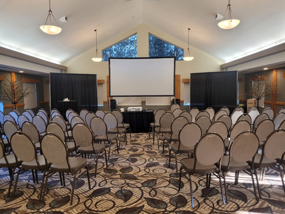 A conference room set up for a presentation with rows of chairs facing a large projector screen.