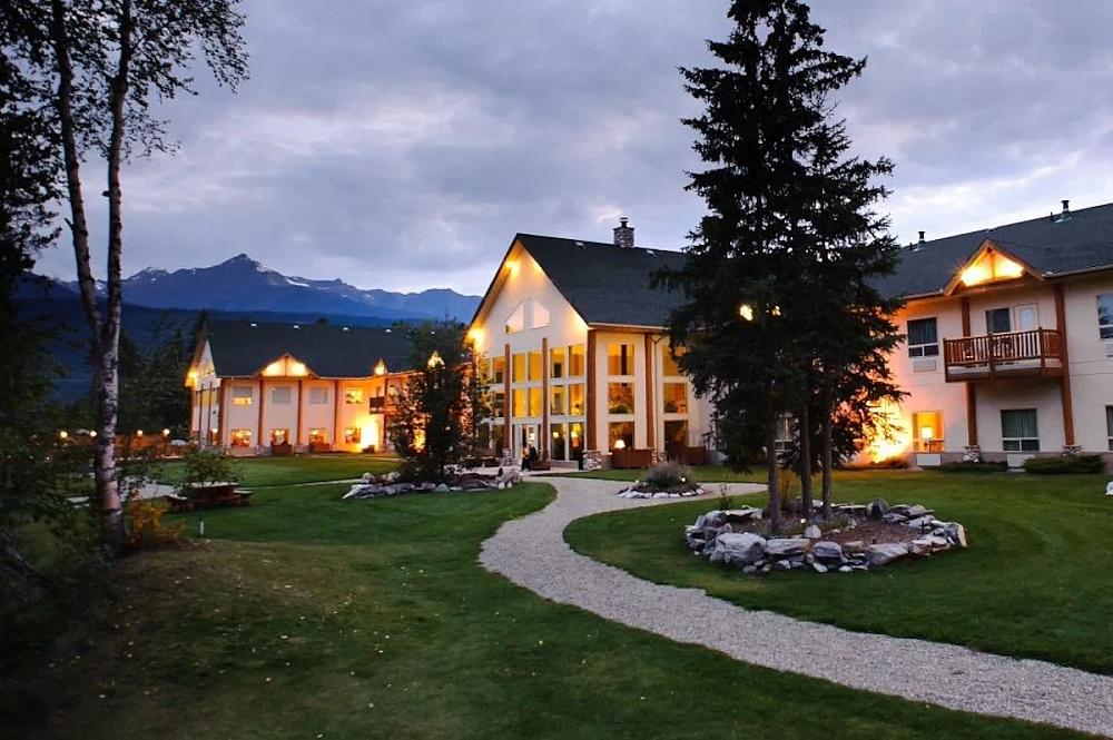 Valemount hotel exterior at dusk with glowing lights, a gravel path, and mountain silhouettes.