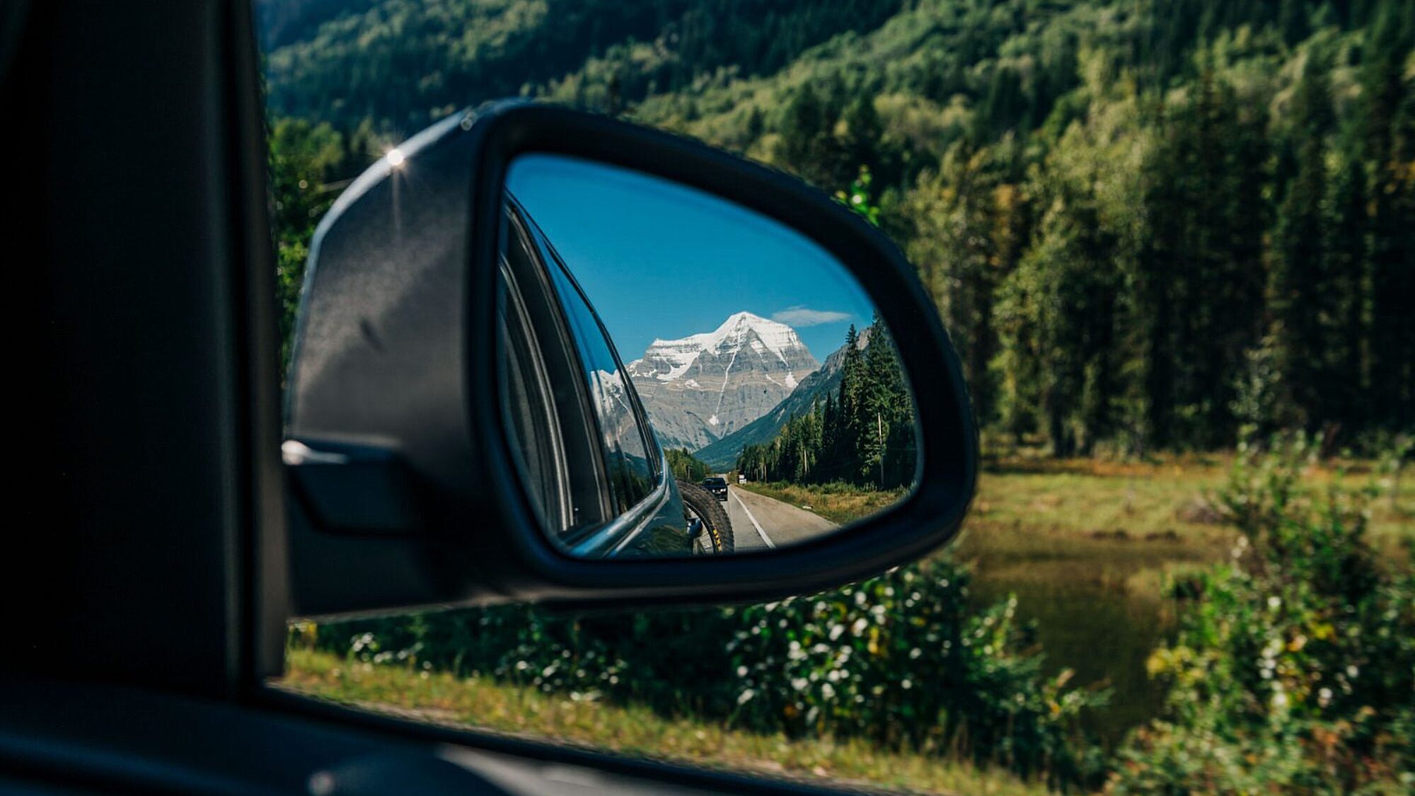 Mountain highway reflected in a car side mirror with forest scenery in Valemount