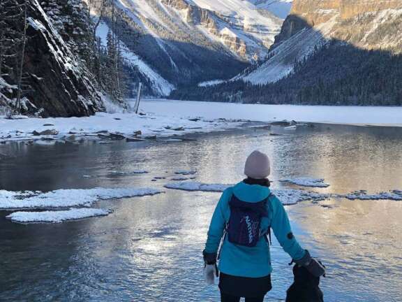 Guest standing with a dog beside the frozen waters of Kinney Lake near Valemount, British Columbia in the winter