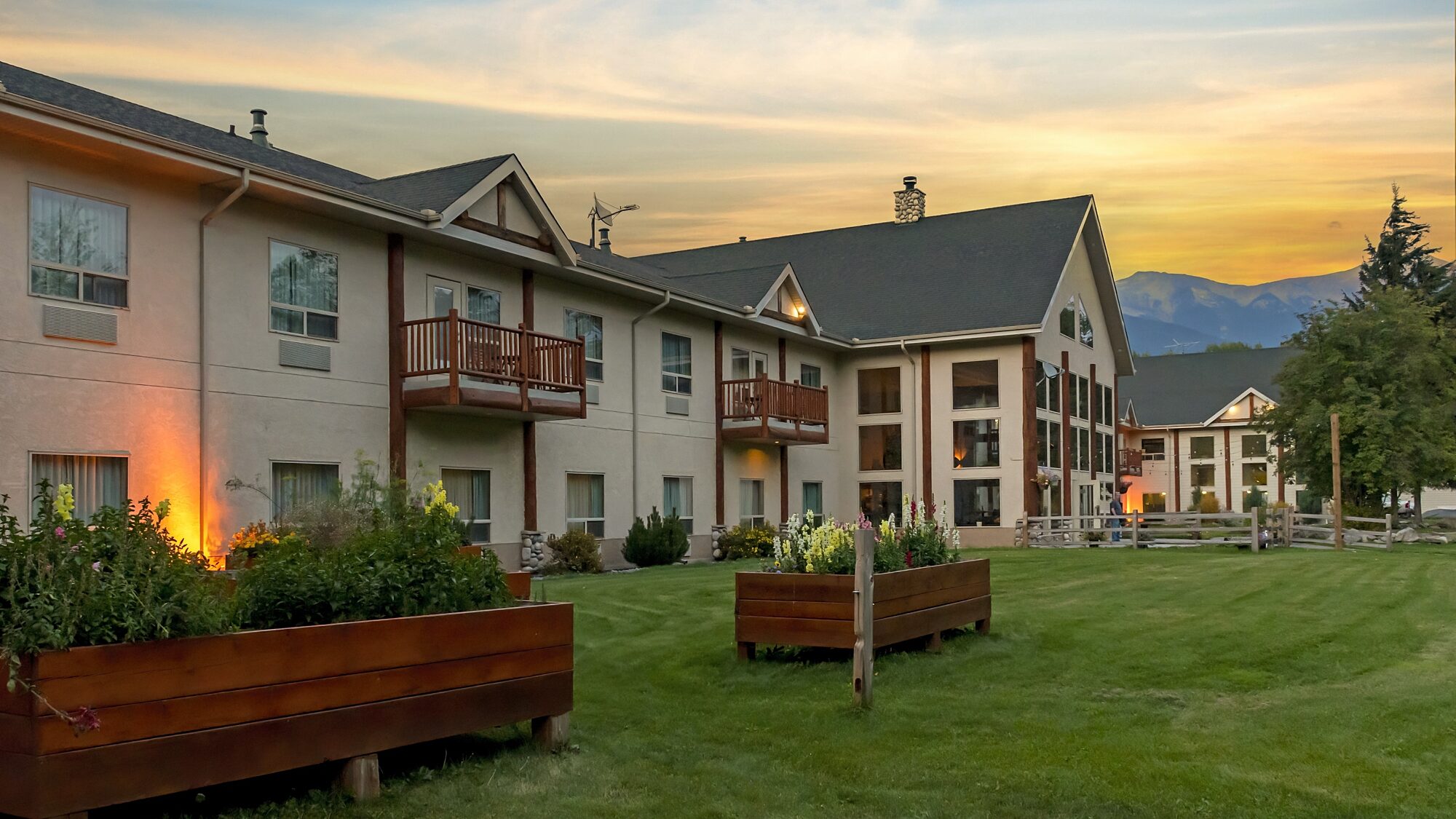 Rear view of Best Western Plus Valemount with balconies, green lawn, and mountains in the background