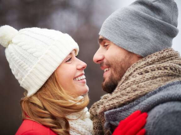 Two guests wearing winter hats and scarves standing outdoors facing each other