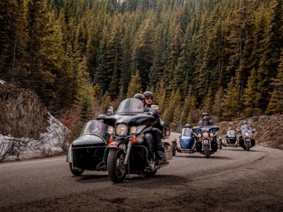 Group riding motorcycles on a forested mountain highway in Valemount
