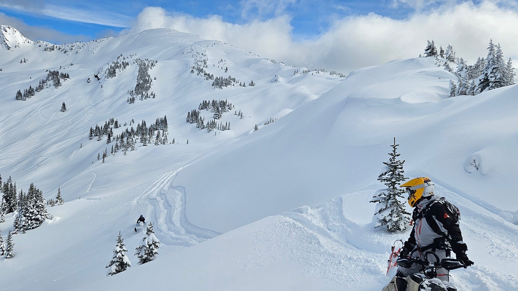 Snowmobiles parked on a snowy mountain ridge with alpine terrain in the background