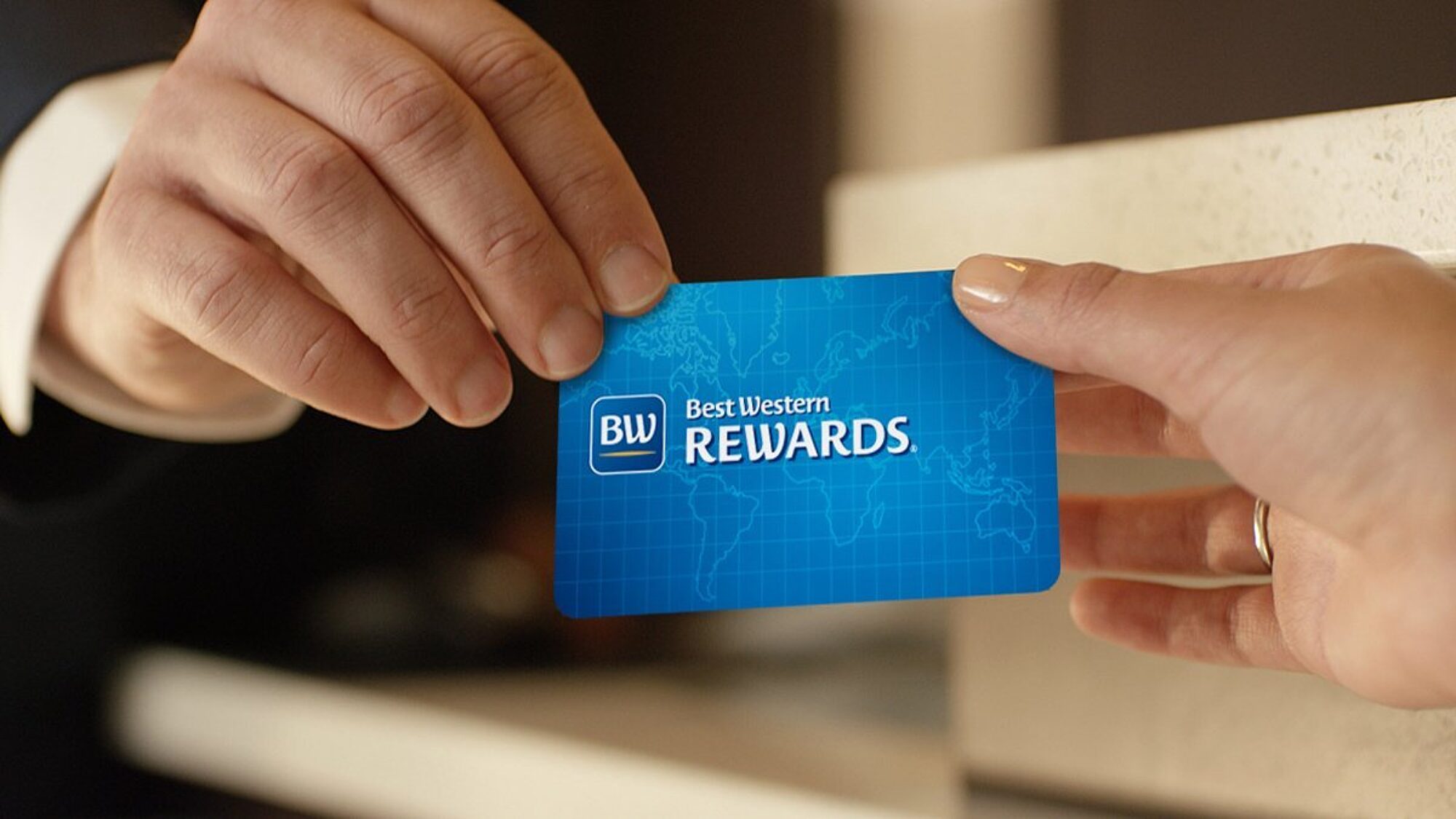Blue card displaying “Best Western Rewards” and BW logo being handed to a guest